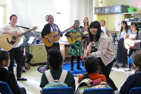 Music therapy students playing guitars for school kids