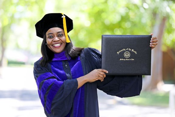 A woman wearing graduation regalia holds a diploma