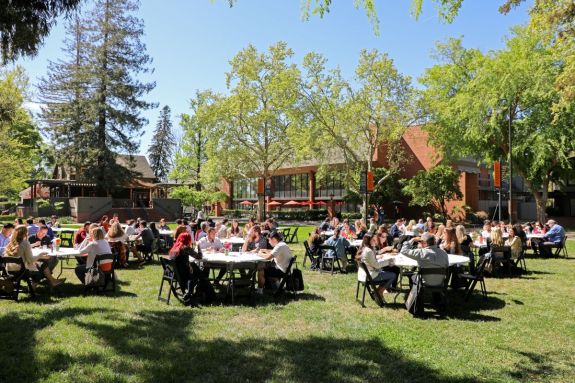 Tables full of people on the campus quad on a sunny day