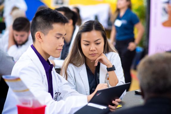 Students in white coats looking at laptop.