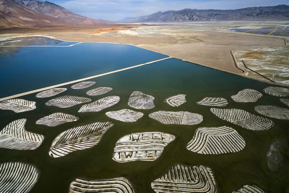 Aerial view of a lake with patterned islands, desert, and mountains in the distance.