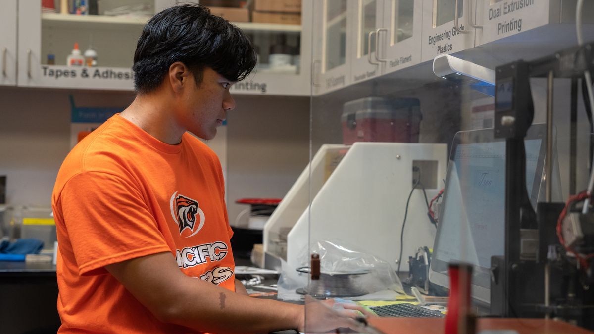 student stands at a 3D printer