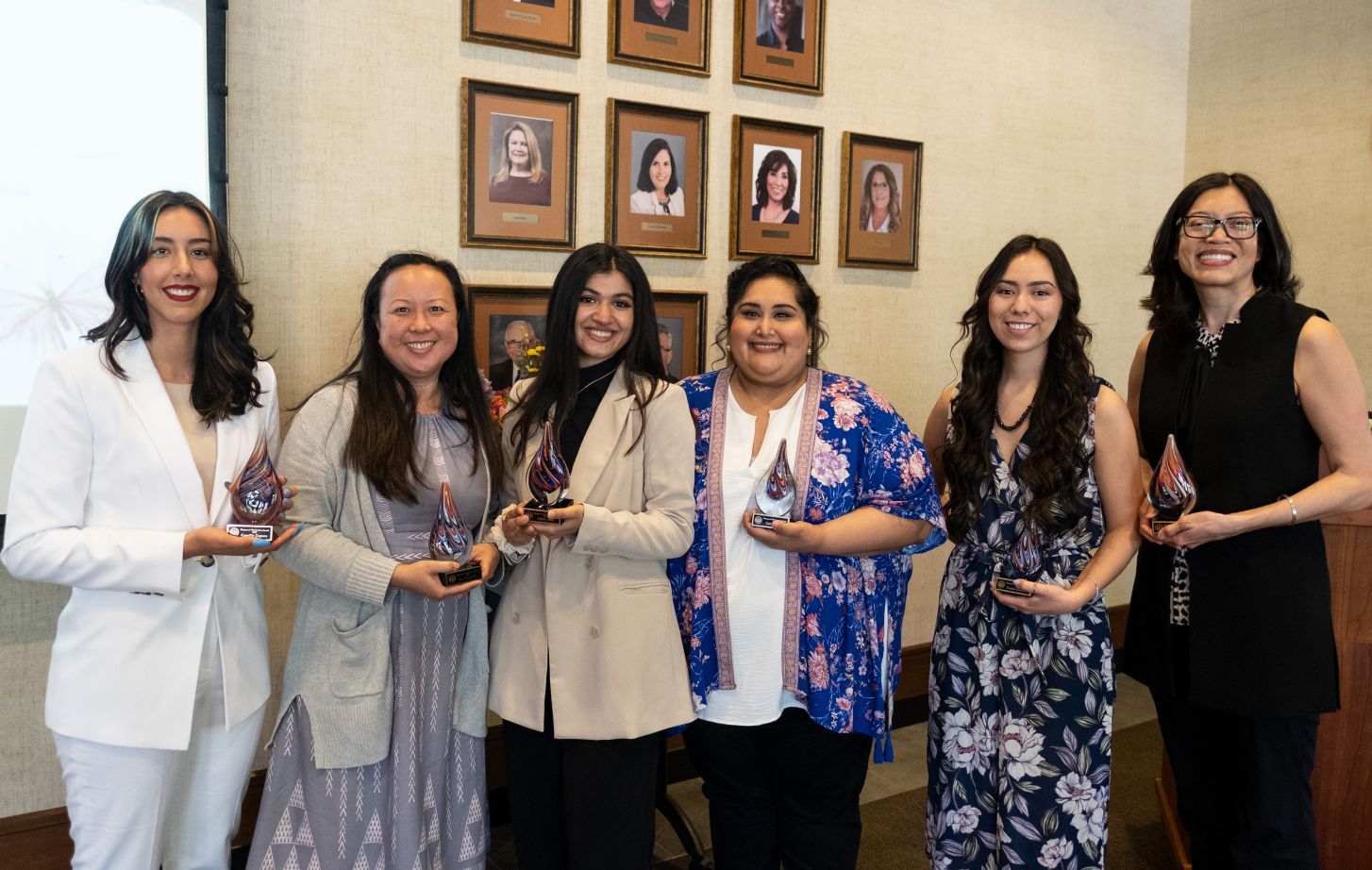Six women stand together holding awards at ceremony