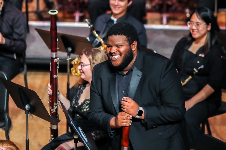 Three musicians smile as they stand on a stage.