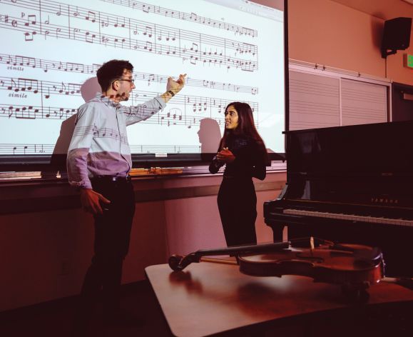 student learning in classroom with teacher pointing at music projected on wall